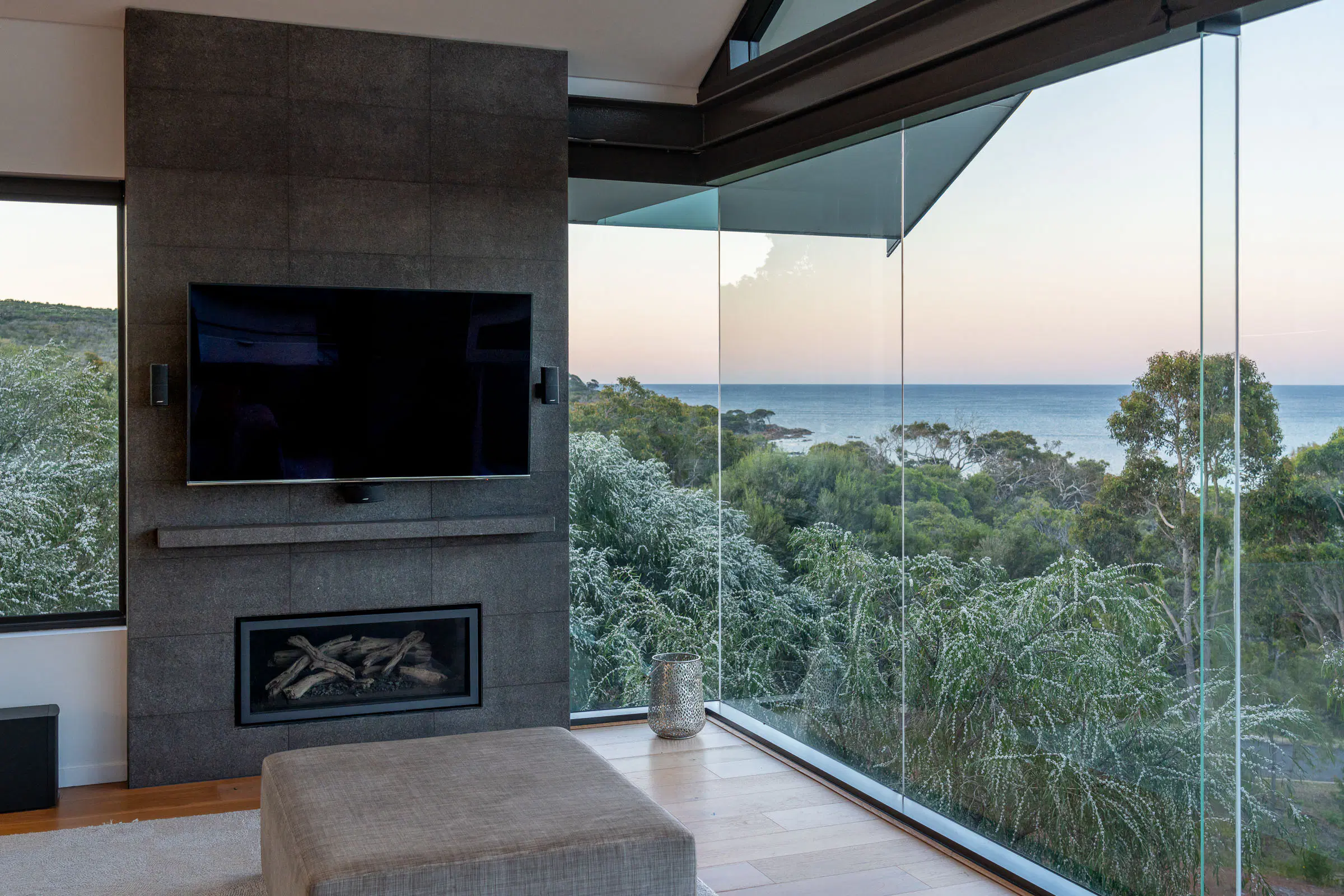 The corner of the living room — fireplace, glass wall, coastal scrub beyond